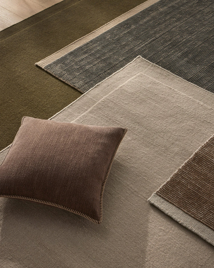 Earthy toned interior styling with Cassio Fog rug, Alba cushion and layered natural textiles in sage green, warm taupe and charcoal with prominent linear weave textures