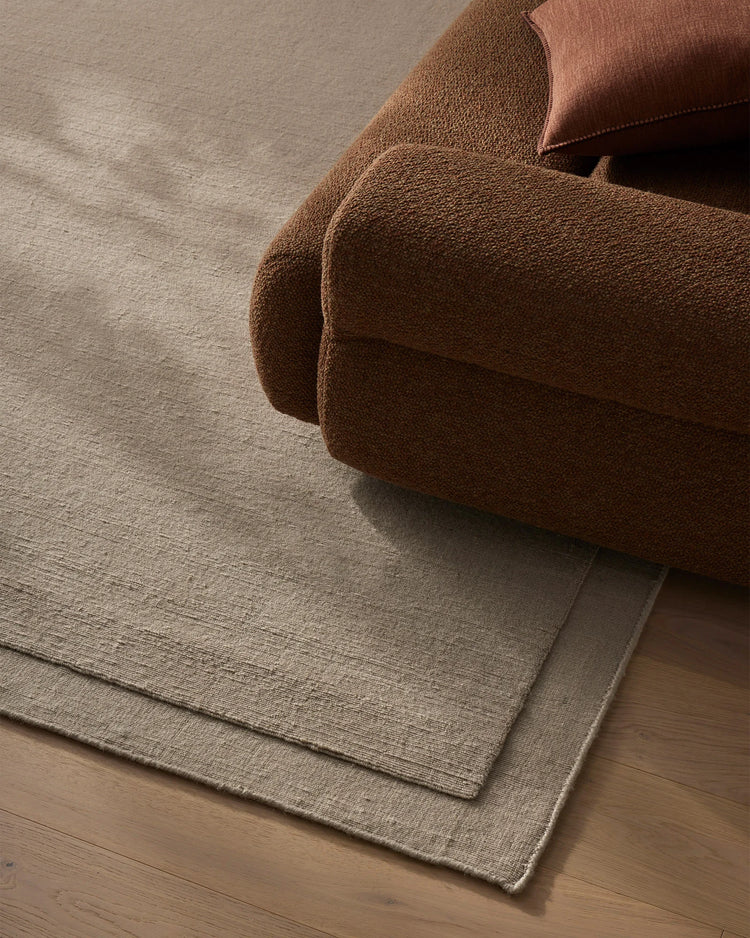 Warm terracotta throw and blush cushion layered over natural wool rug in neutral grey, showcasing textured weave and warm earth-tone palette for understated living room styling