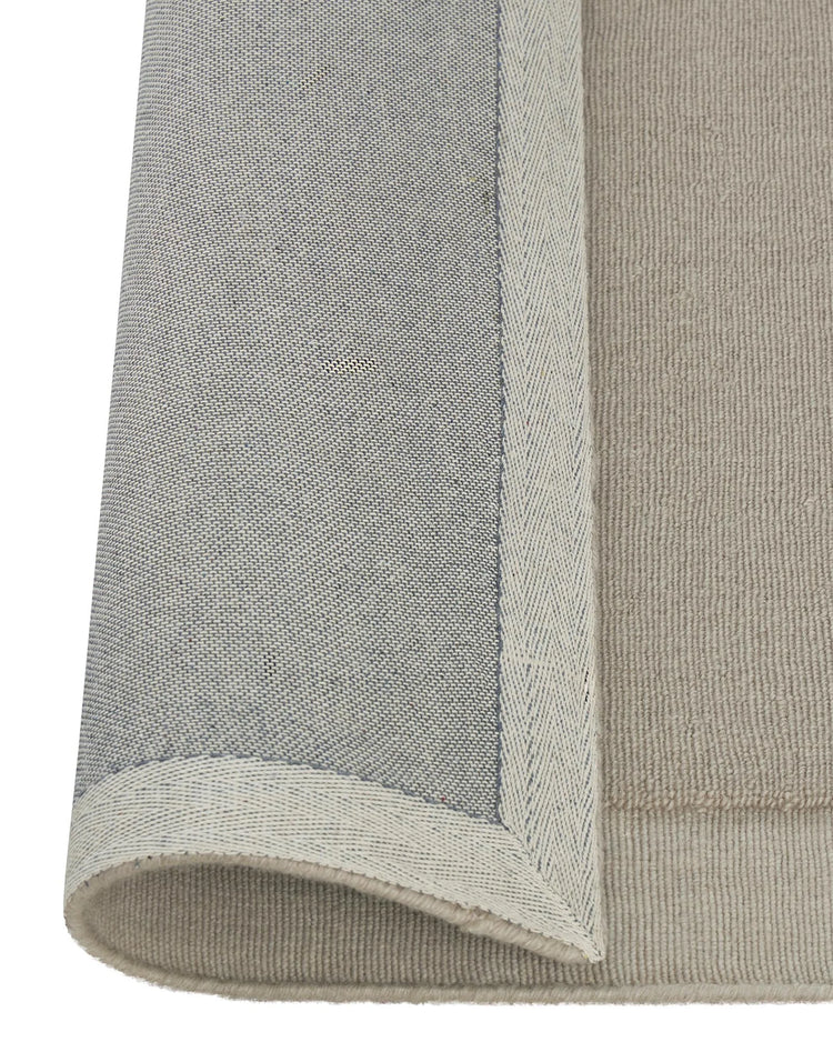 Cassio Fog rug detail showing tightly woven NZ wool loop pile with serged edge border in soft ecru by Weave Home