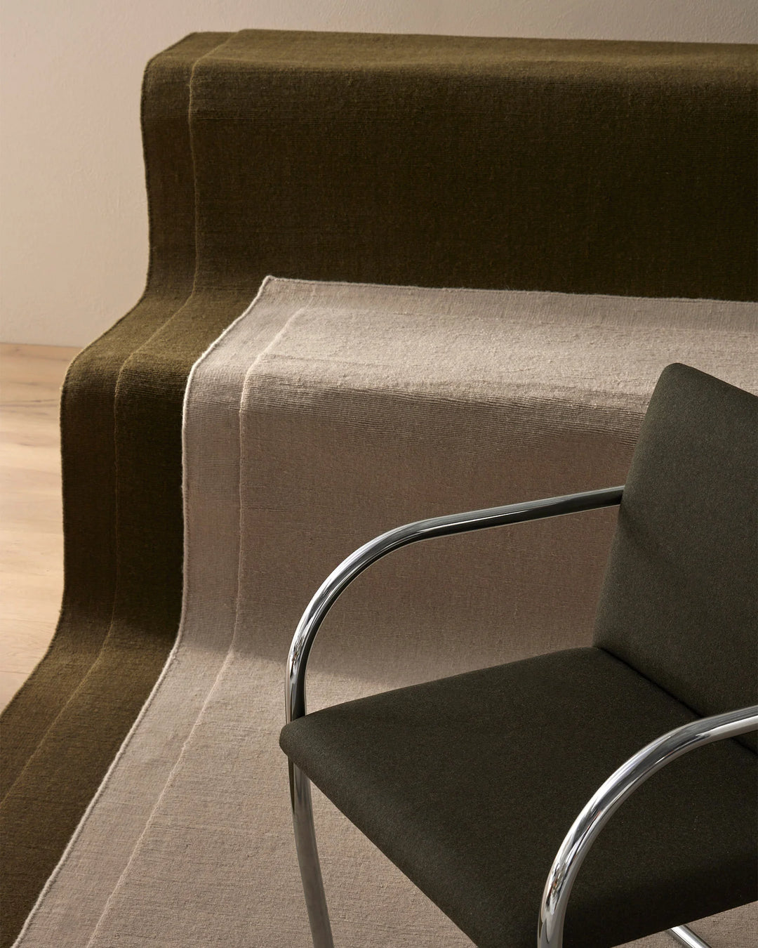 Earthy toned living space with layered Cassio rugs in sage and charcoal, paired with modern chrome chairs on natural timber flooring