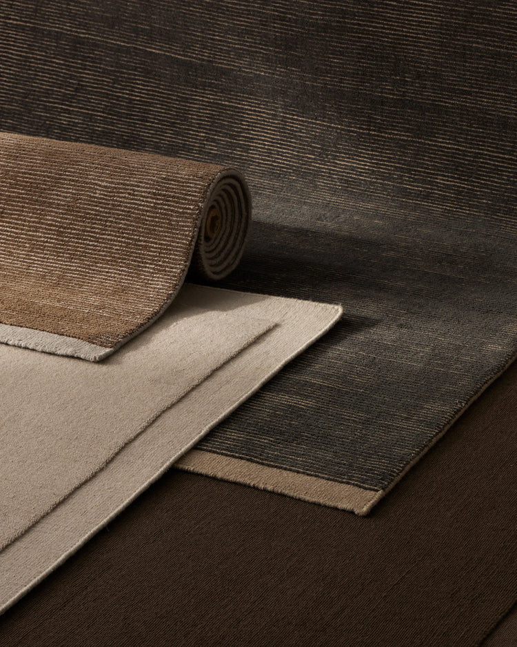 Layered wool rugs in charcoal, taupe and sand tones showcase textured ribbed weave and natural fibre depth in neutral interior styling