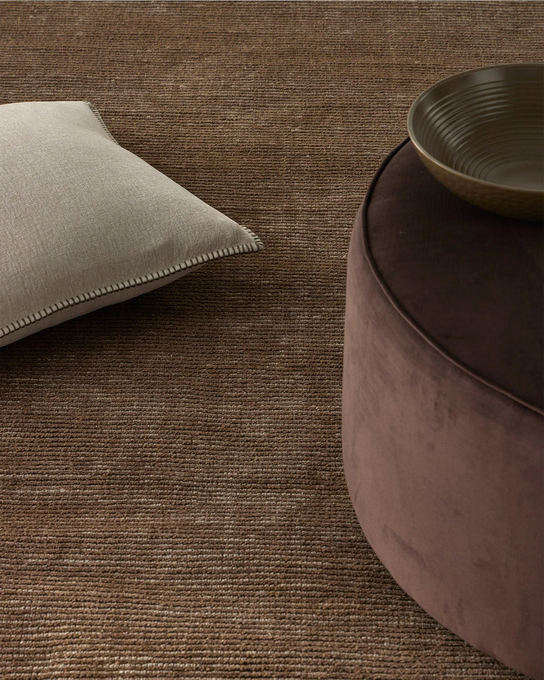 Warm minimalist interior styling neutral palette: Alba Bone cushion on textured Remo Earth wool rug with charcoal ceramic vessel, earthy tones and woven textures