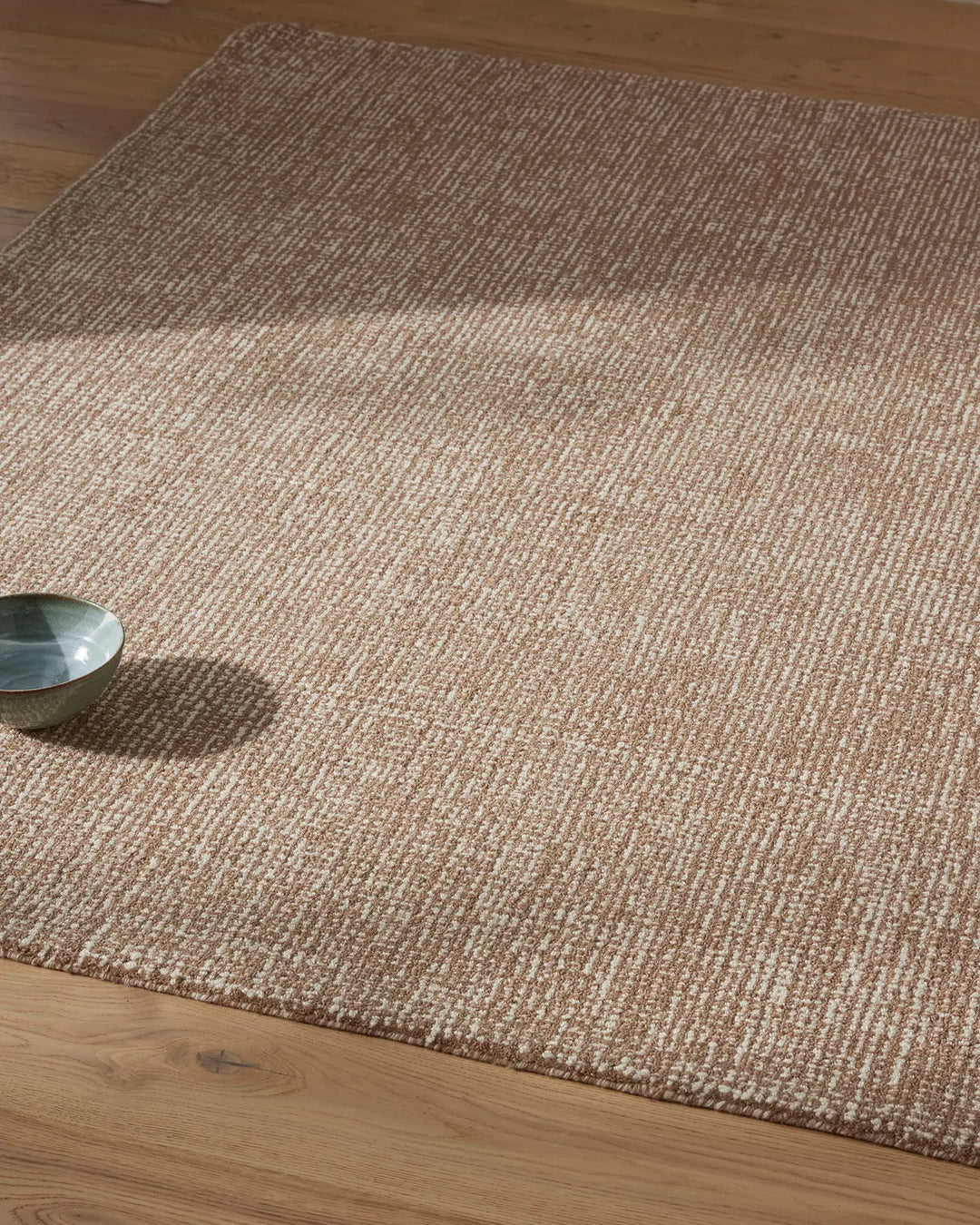 Neutral wool rug with ribbed texture in mocha and cream tones, layered on light timber flooring with minimalist styling and natural daylight
