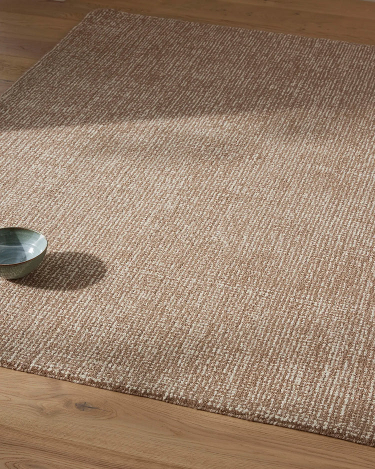 Neutral wool rug with ribbed texture in mocha and cream tones, layered on light timber flooring with minimalist styling and natural daylight