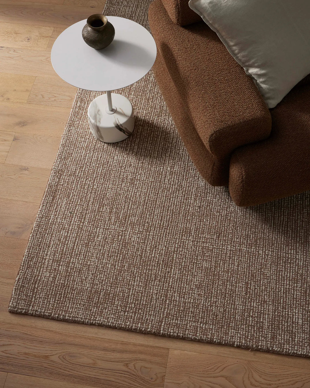 Neutral living room with beige wool rug, warm brown linen sofa, white side table and natural wood flooring—earthy palette with textural layering