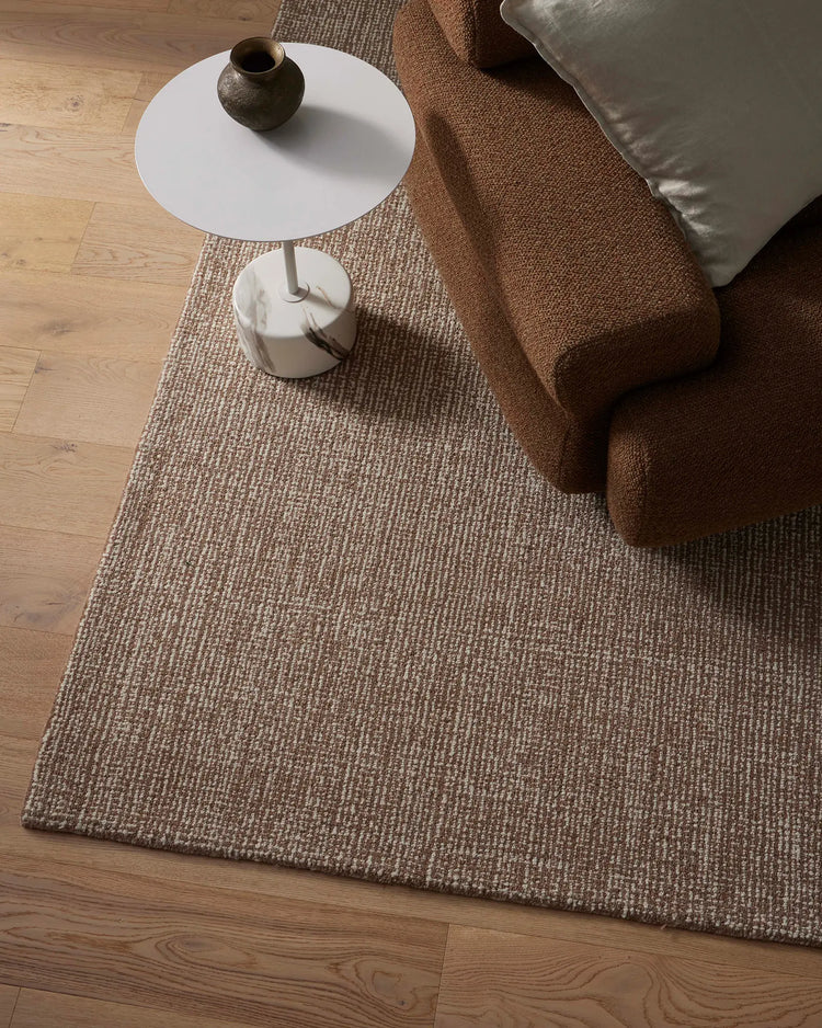 Neutral living room with beige wool rug, warm brown linen sofa, white side table and natural wood flooring—earthy palette with textural layering