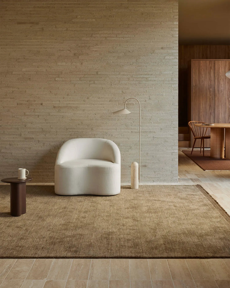 Neutral minimalist living space styled with a cream armchair and walnut-toned area rug anchoring a cream brick wall, warm wood accents, and sculptural lighting.