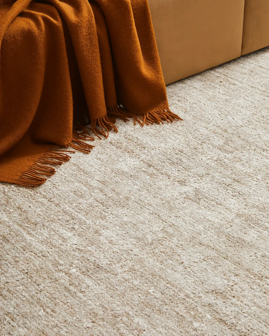 Warm terracotta wool throw with fringe draped over neutral sofa, styled on textured cream and opal natural fiber rug for earthy, minimalist home décor