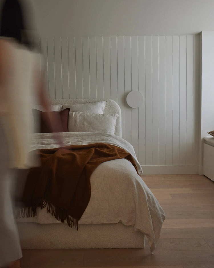 Minimalist bedroom with warm terracotta throw and cream linen bedding layered on neutral base, vertical shiplap headboard, earthy palette with natural textures
