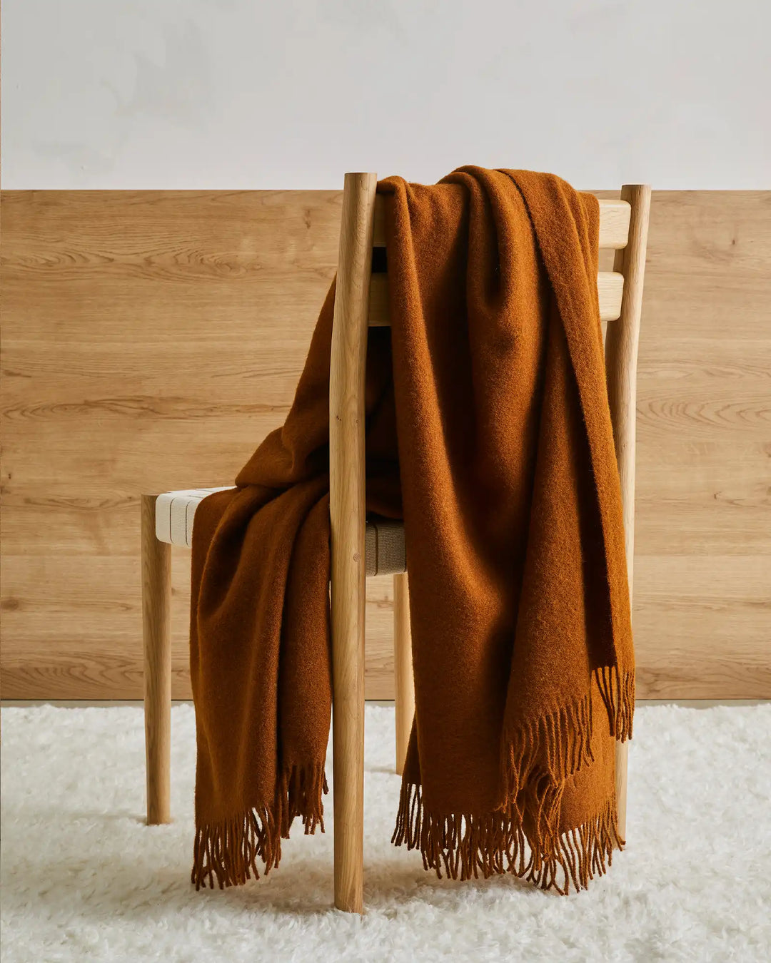 Nevis Spice wool throw in burnt orange draped over wooden chair, showing tassel fringe detail by Weave Home