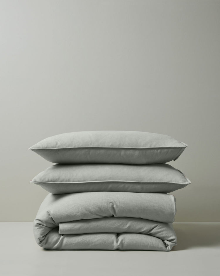 Stacked linen bedding in soft sage tones: Ravello Quilt Cover and Ravello Pillowcase set layered together, showcasing natural texture and neutral minimalist aesthetic