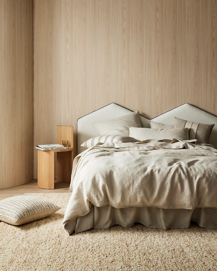 Serene bedroom with natural linen bedding in cream and taupe, wood-panelled walls, neutral wool rug, and linen cushions in warm earthy tones