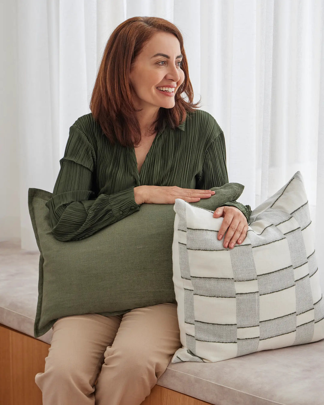 Fiore Olive lumbar and square cushions in linen viscose blend, stacked and displayed on a bed, showing soft sage green and natural cream tones by Weave Home
