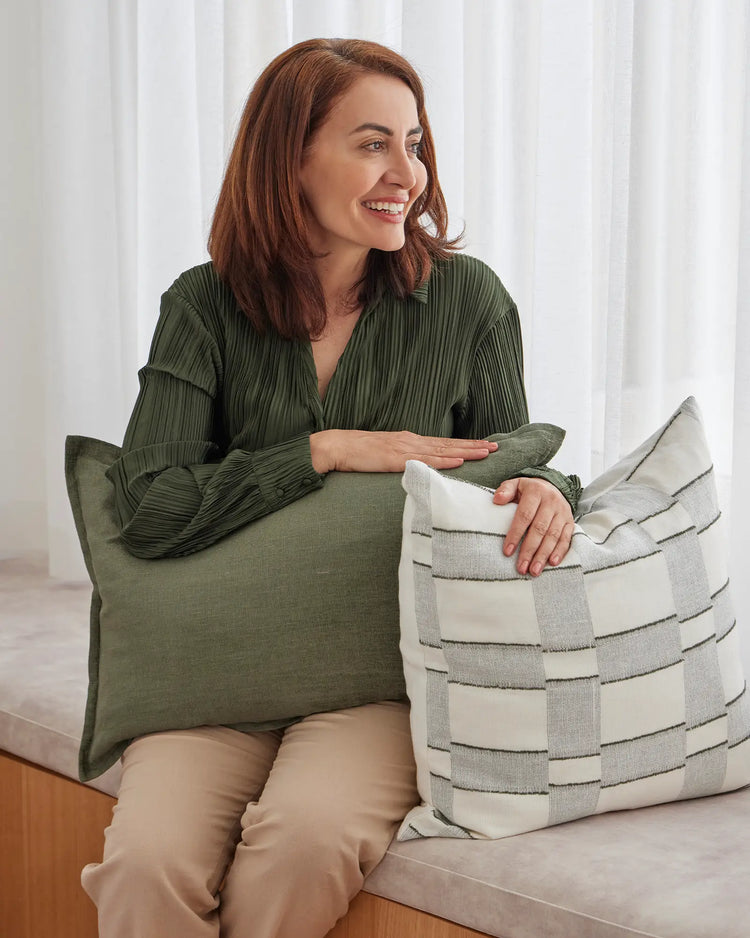 Fiore Olive lumbar and square cushions in linen viscose blend, stacked and displayed on a bed, showing soft sage green and natural cream tones by Weave Home