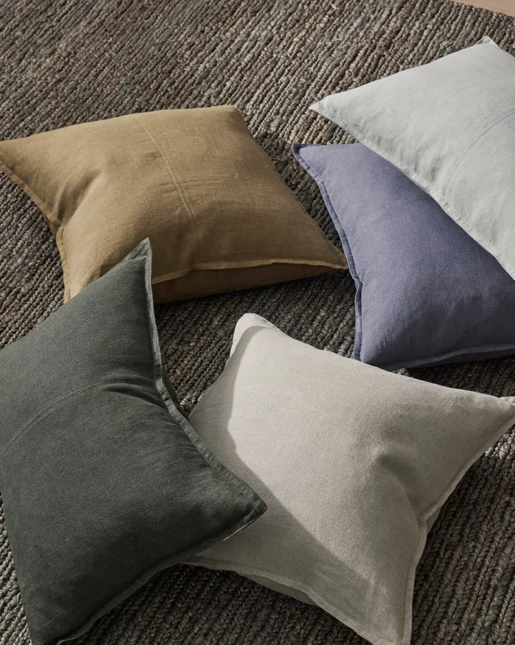 Neutral linen cushions in sage, stone, cream and lavender arranged on textured grey wool rug, showcasing Como range in earthy, calming palette