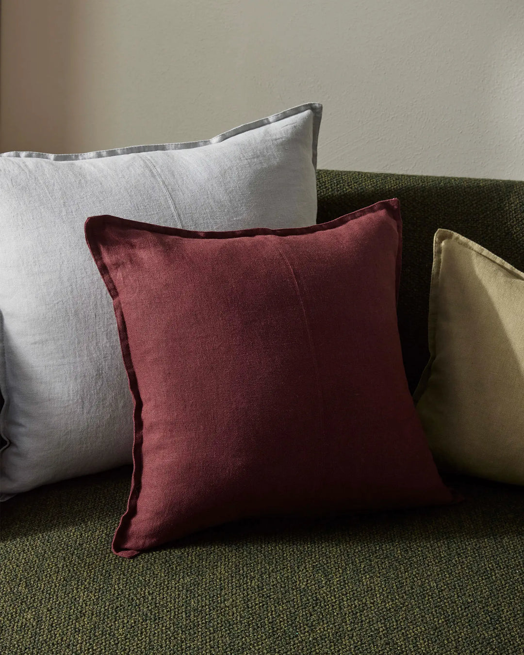 Sage green upholstered sofa styled with linen cushions in garnet, haze grey, and chartreuse, creating an earthy, layered palette with textural contrast