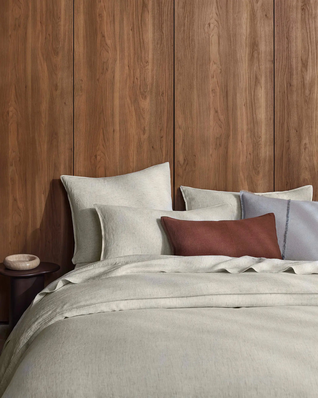Warm timber bedroom with natural linen bedding in cream tones, styled with terracotta and haze cushions for earthy, minimalist bedroom decor