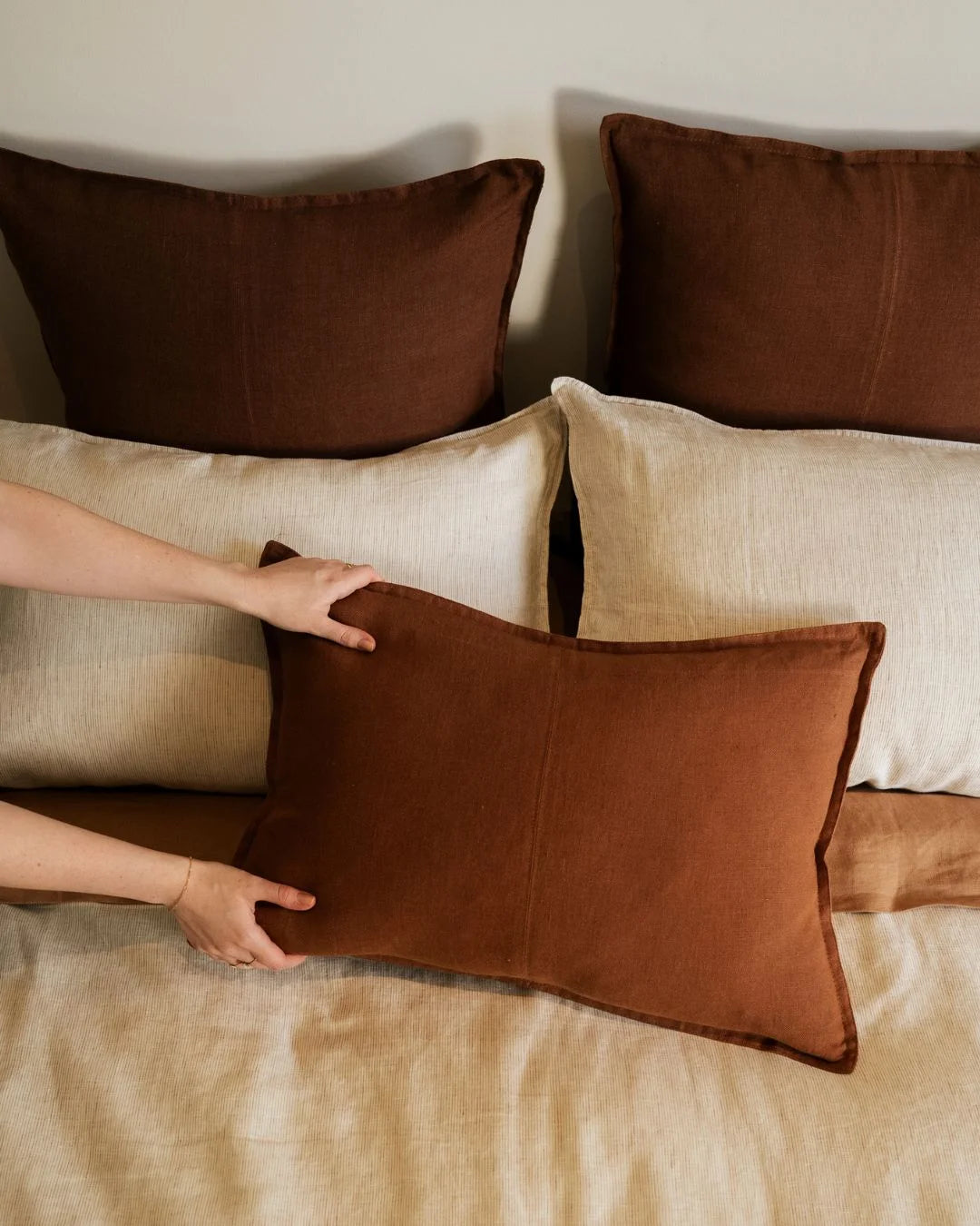 Warm earth-tone bedding styled with linen pillows in chocolate brown and natural cream, textured finishes creating layered comfort aesthetic