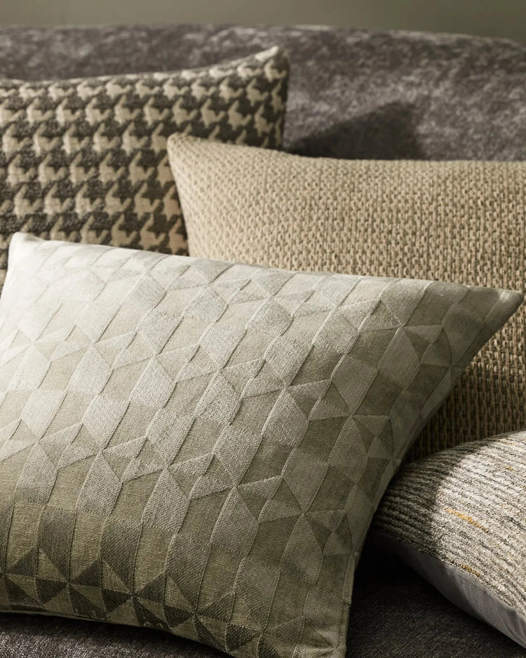 Neutral layered cushions in sage and cream linen blends styled on a sofa, featuring quilted geometric textures and woven patterns in warm greige tones