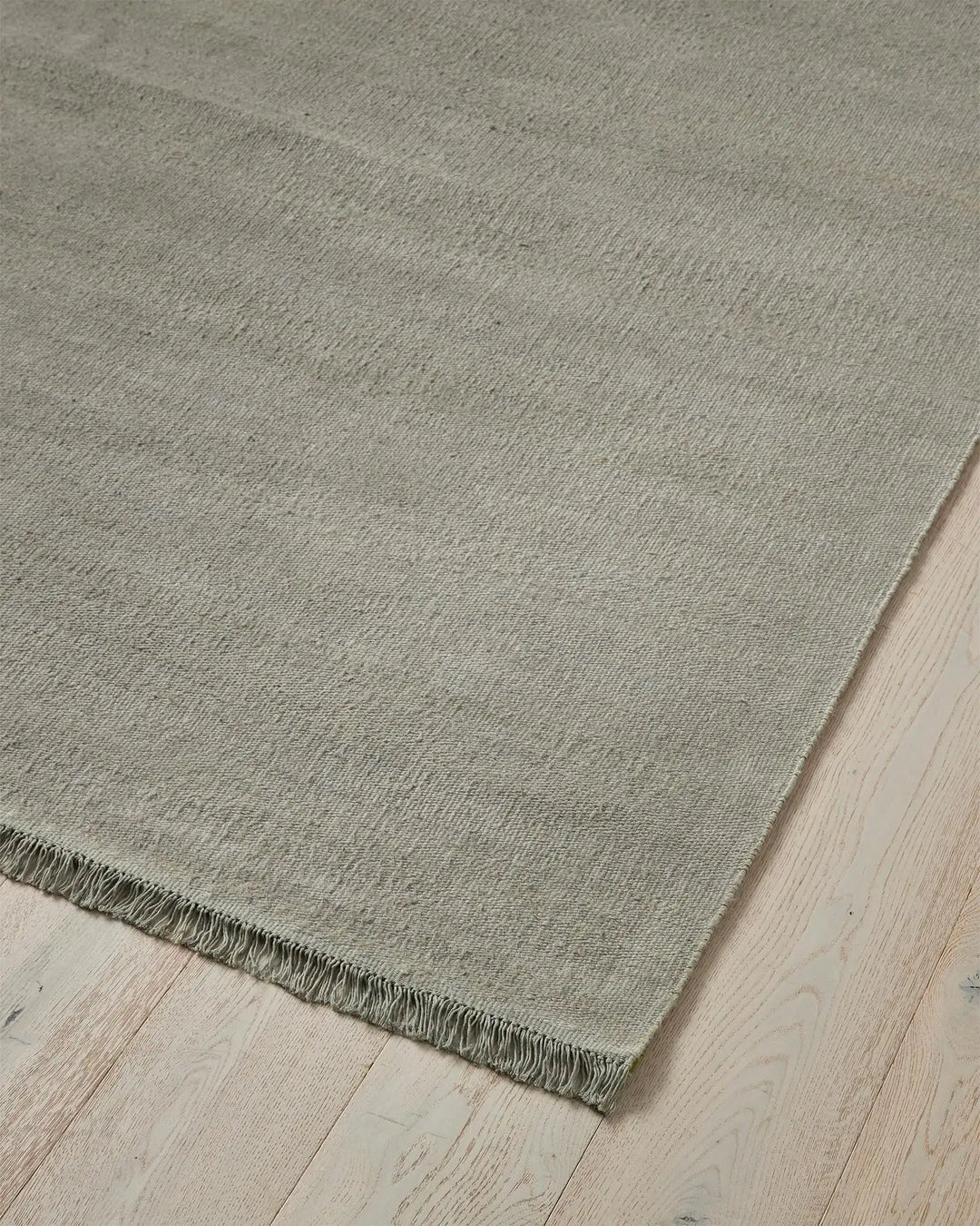 Emilio Flint linen rug corner detail, showing soft grey-blue flat-weave with fringe edge by Weave Home