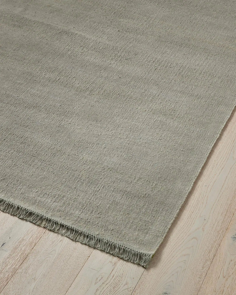Emilio Flint linen rug corner detail, showing soft grey-blue flat-weave with fringe edge by Weave Home