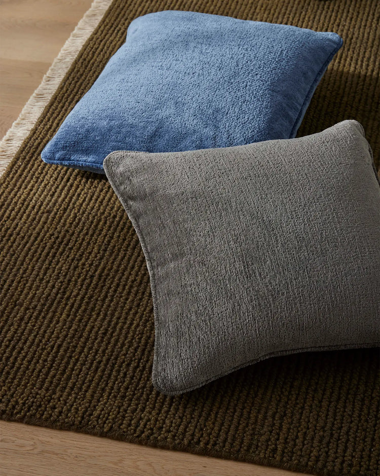 Blue and grey Tempo cushions on olive ribbed rug, earthy tonal styling with textured woven surfaces and natural light
