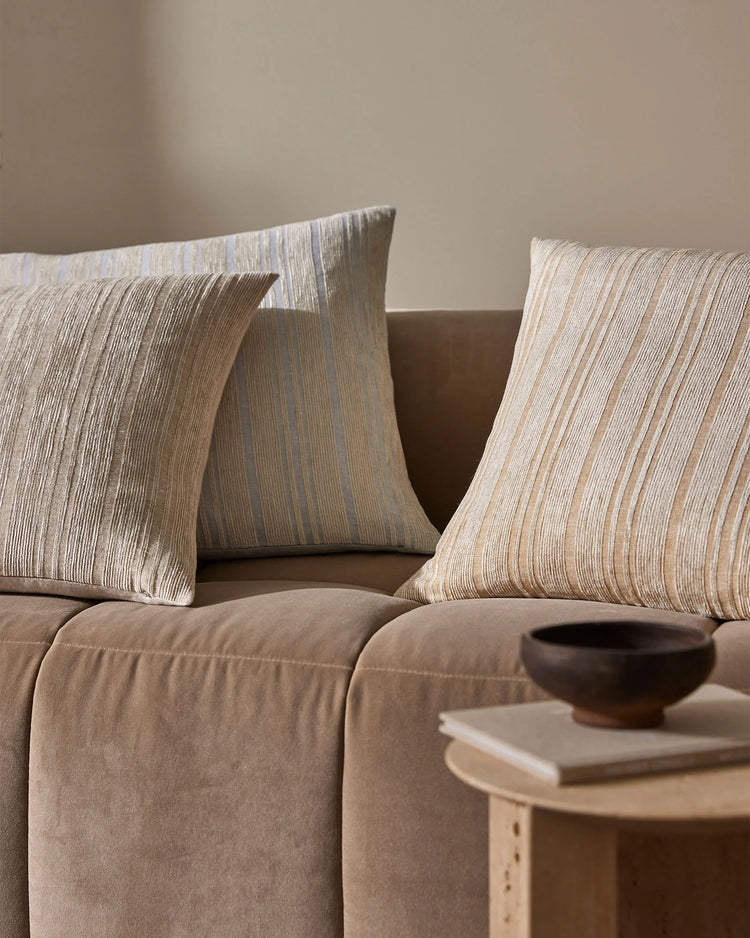 Neutral striped linen cushions styled on a taupe sofa with warm wood side table, minimalist aesthetic with earthy tones and natural textures