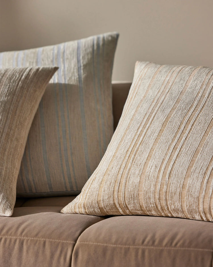 Neutral linen cushions with fine vertical texture layered on taupe sofa, warm natural light casting soft shadows across woven surface
