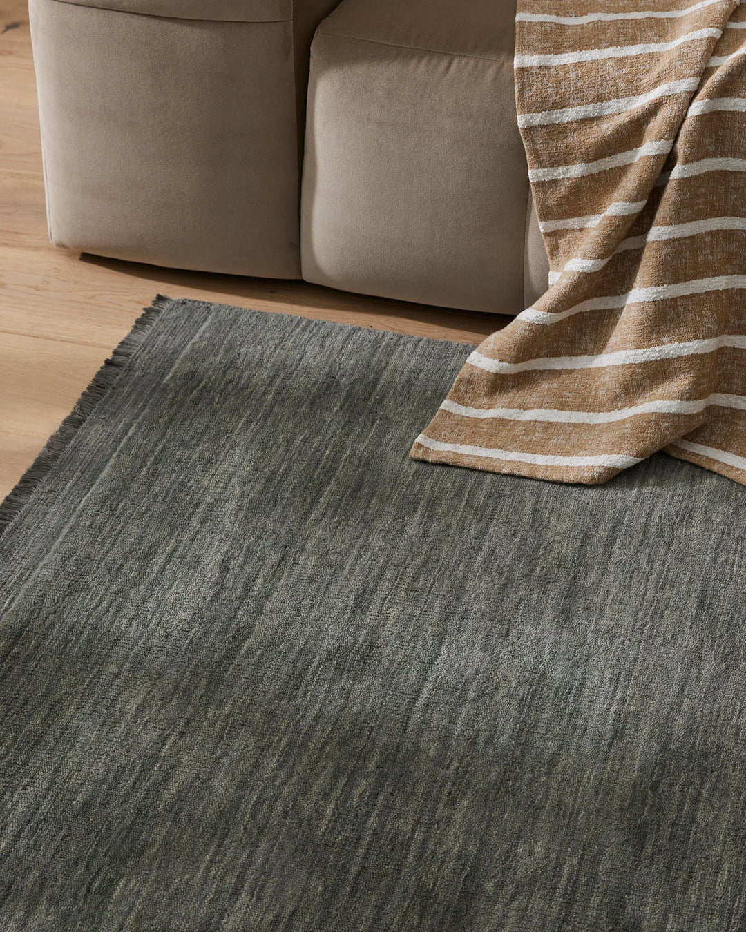 Neutral living room styled with sage striped throw and beige upholstered seating on textured grey-green Silvio rug with natural linen textures throughout