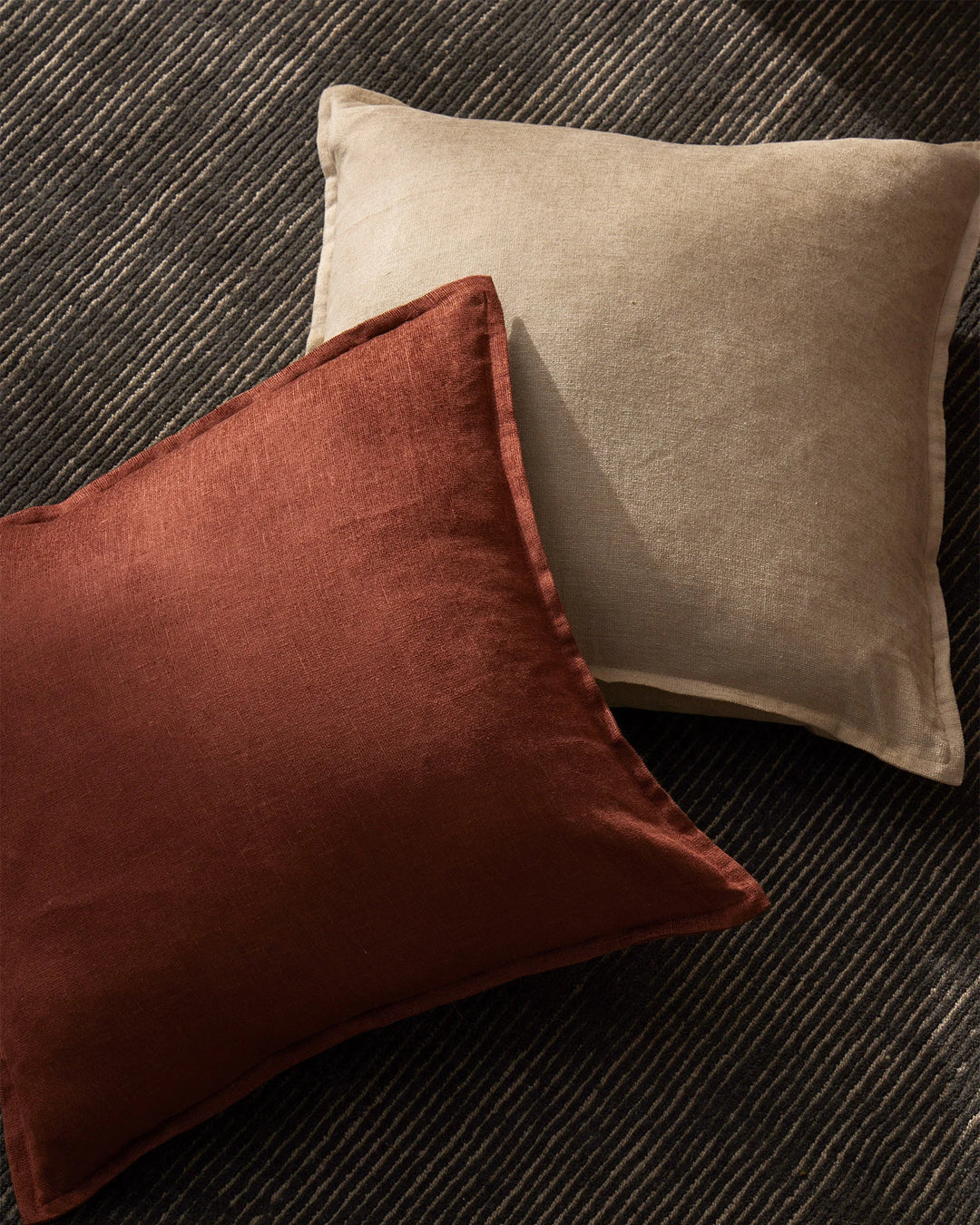 Earthy neutral and terracotta cushions layered on a charcoal wool rug, showcasing warm earth tones and linen-viscose textures in modern interior styling