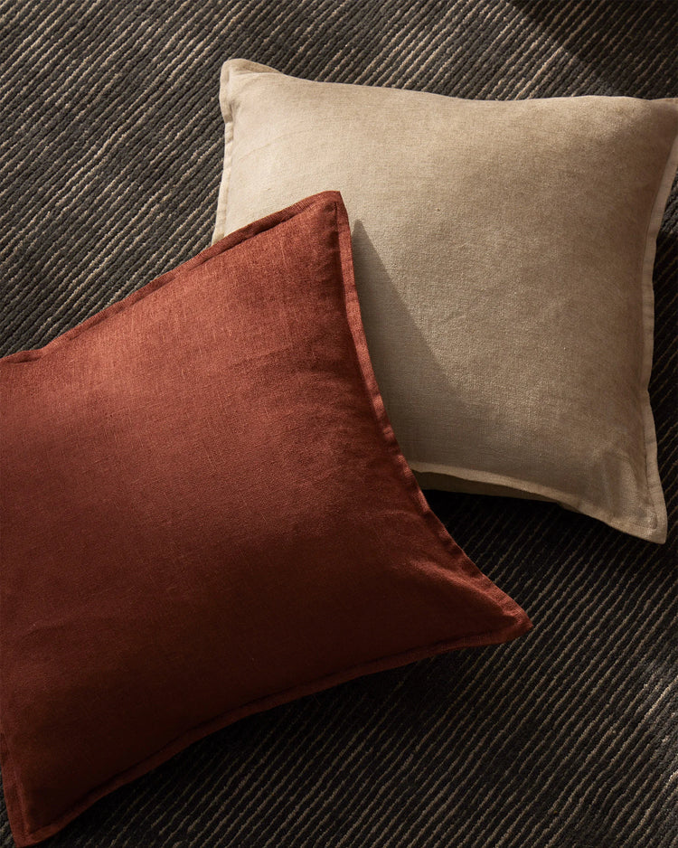 Earthy neutral and terracotta cushions layered on a charcoal wool rug, showcasing warm earth tones and linen-viscose textures in modern interior styling