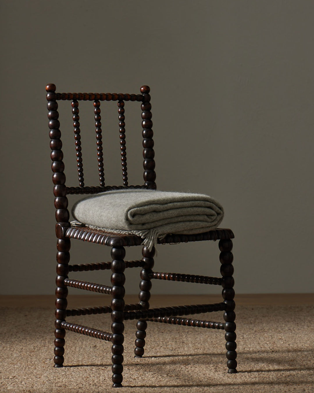 Nevis Ash throw in light steel grey lambswool, folded on wooden spindle chair, tassel border detail visible by Weave Home