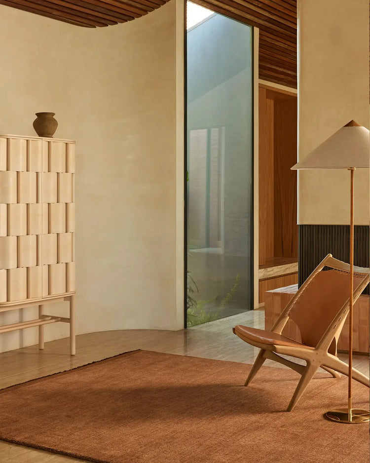 Warm terracotta rug anchoring a minimalist mid-century living space with cream walls, wooden furnishings, and soft overhead lighting; Silvio in Sienna.