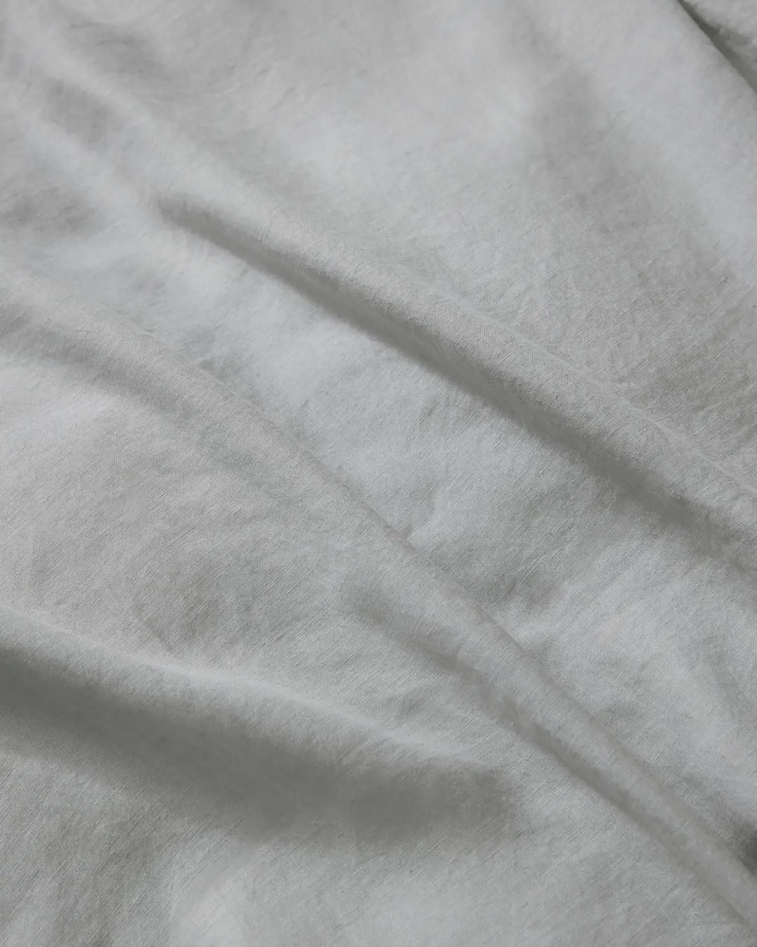 Close-up of silver Ravello flat sheet showing soft crumpled linen texture and natural light play on neutral bedding fabric
